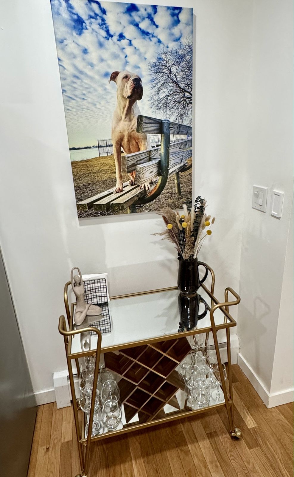 Gold bar cart with wine glasses under a photograph of a dog on a bench