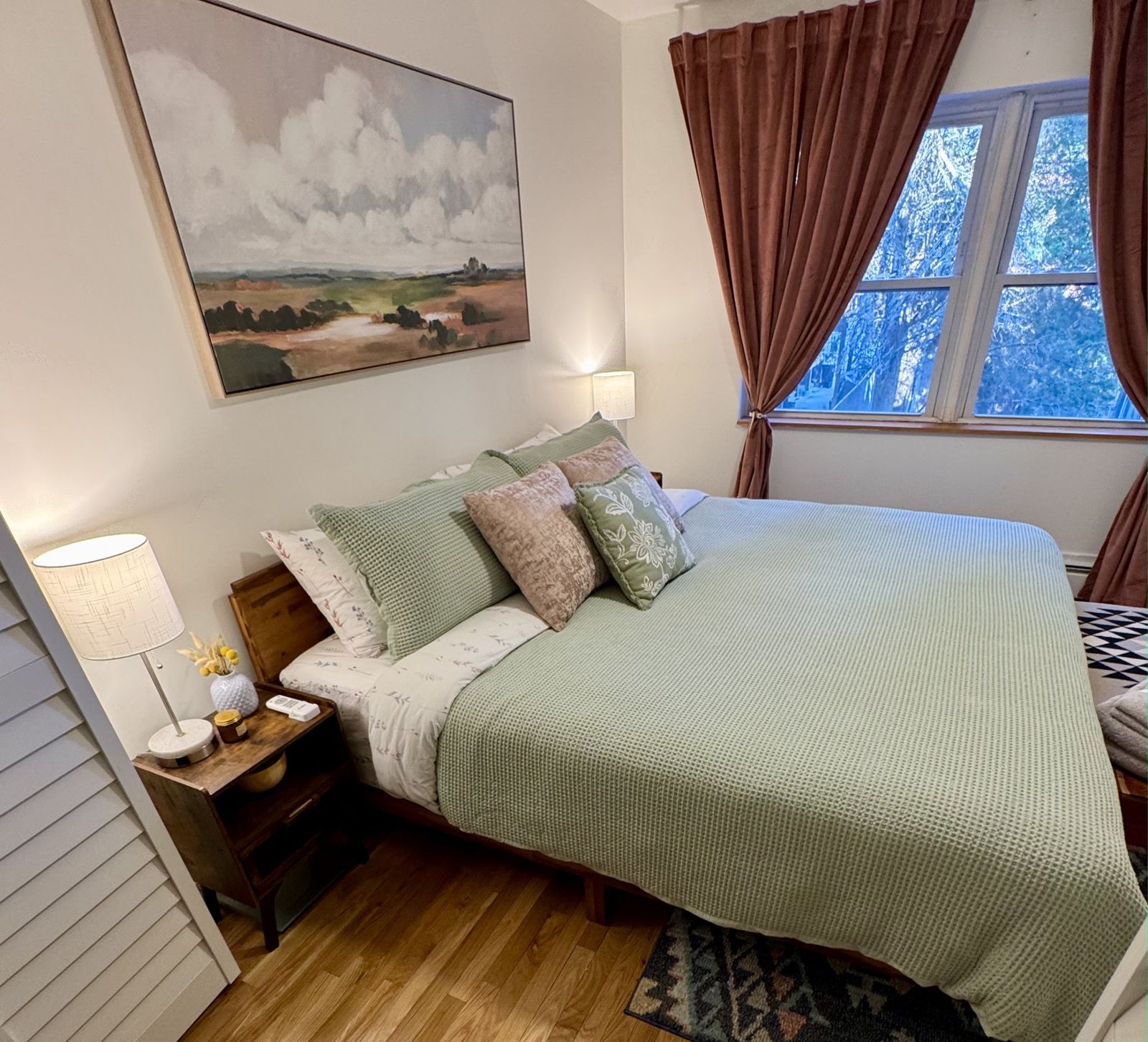 Primary bedroom with a king bed in sage green bedding under a cloud landscape painting