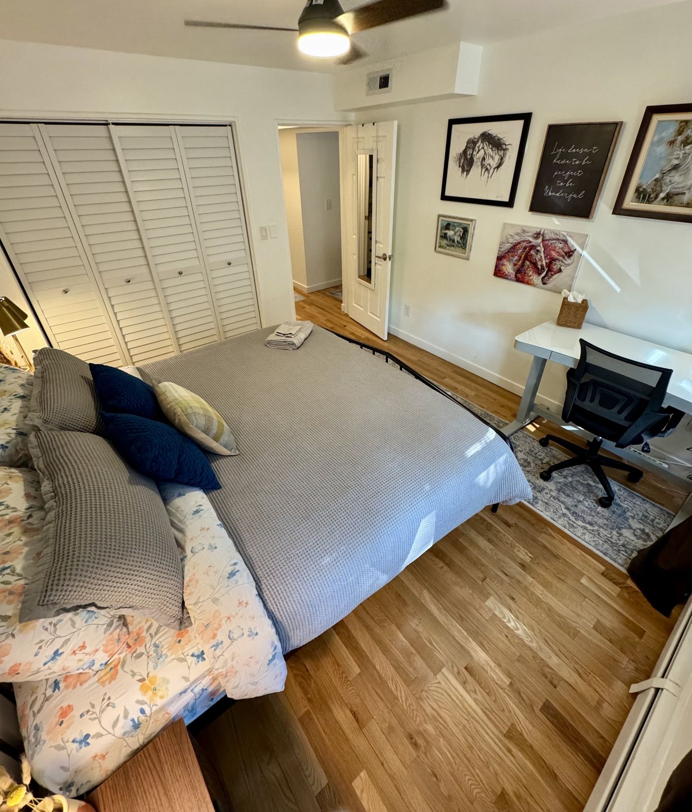 The same bedroom from the bed, showing the standing desk, chair and framed art