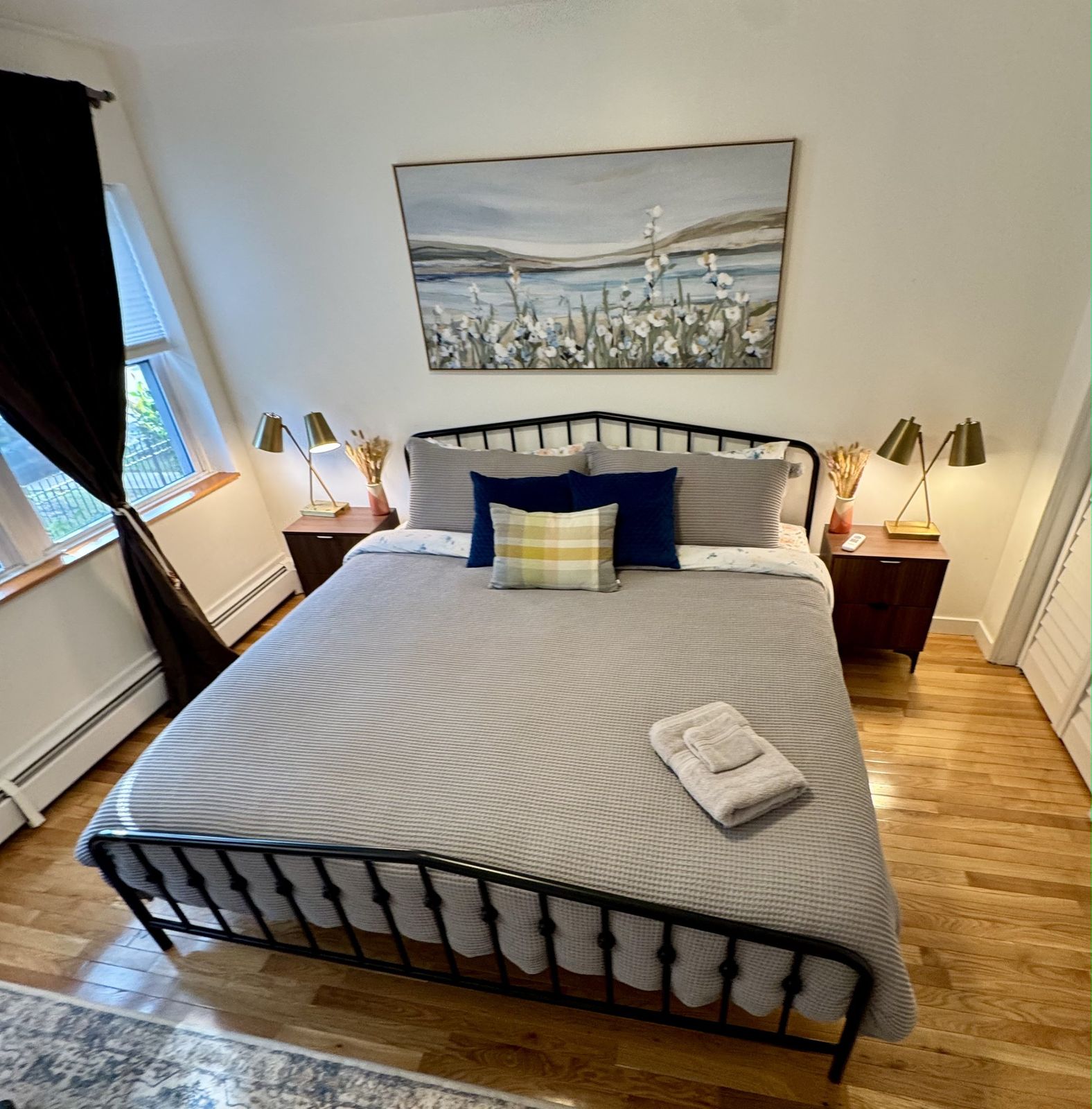 Bedroom with a king bed in grey bedding, navy pillows and a painting of white flowers