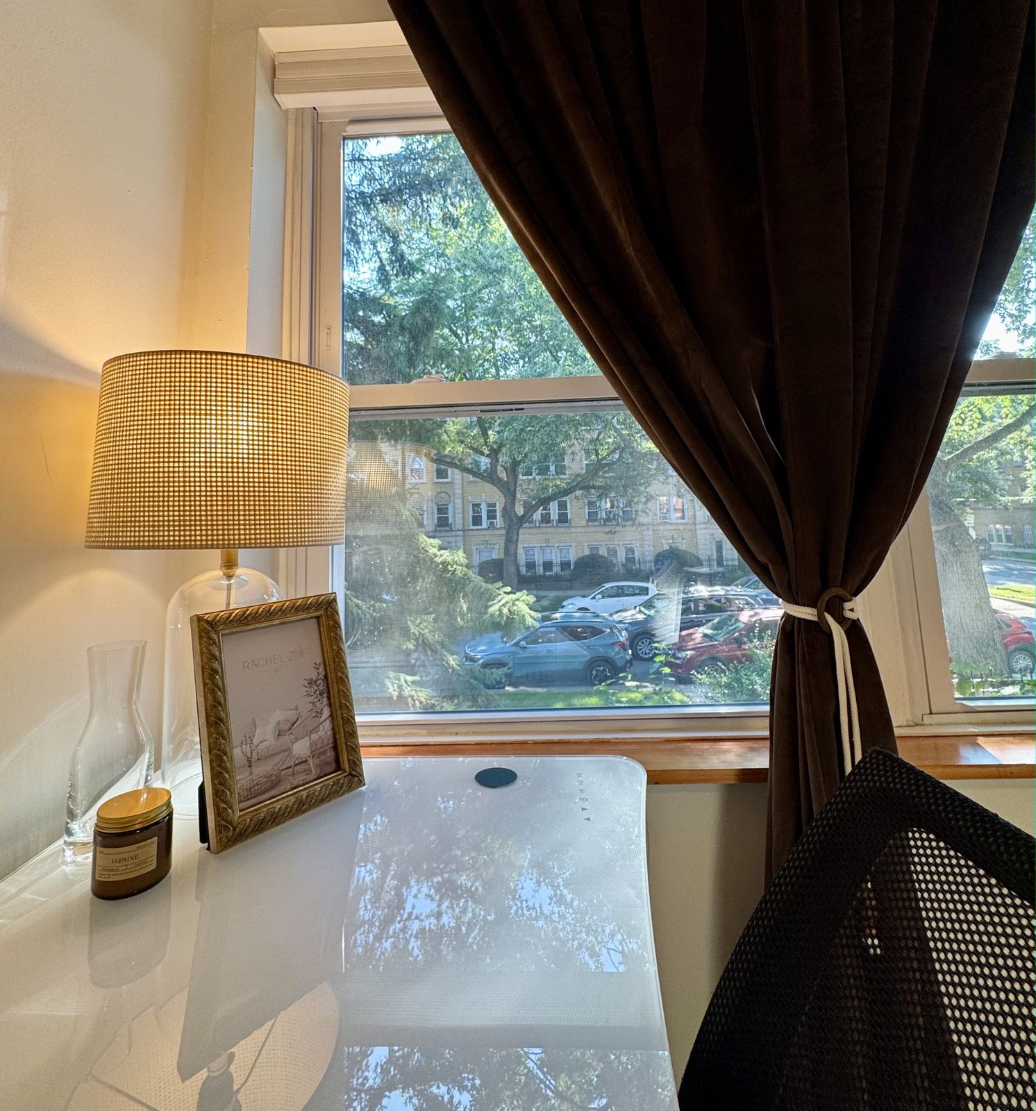 Glass topped desk with a lamp, looking out the window onto a tree lined street