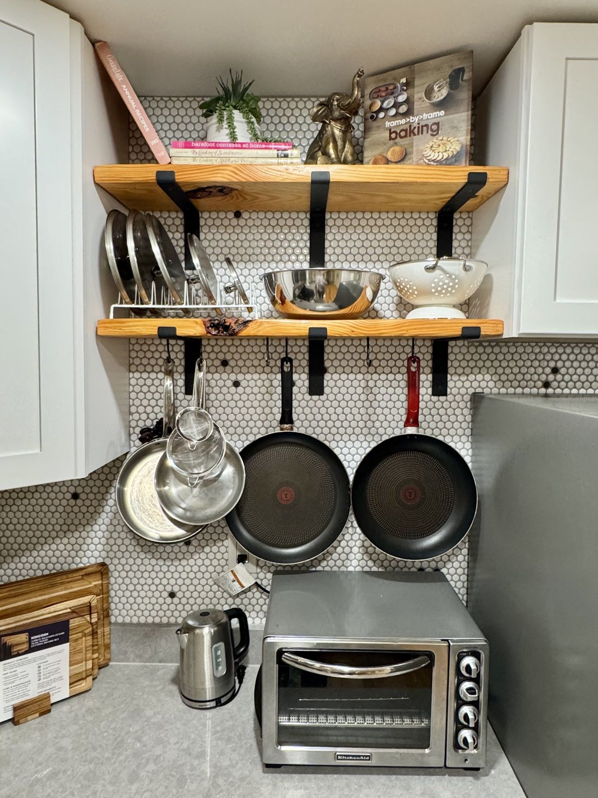 Open wooden shelves with cookbooks, pans hanging below and a toaster oven