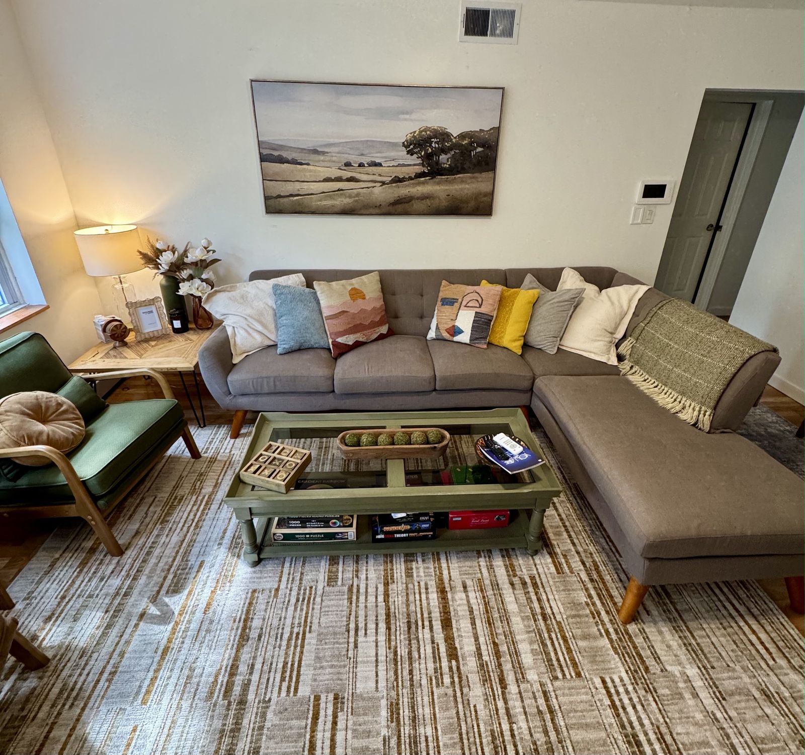 Living room with a grey sectional sofa, a green coffee table and a landscape painting above